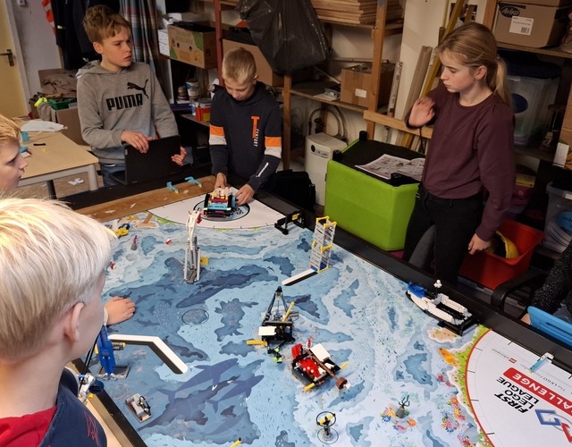 Kampioenen First Lego League Friesland 2025 cbs it fundamint hallum groep 8 kinderen juichen groep kinderen en volwassenen in rode teamuniformen vieren feest op een podium met medailles, een certificaat en een trofee