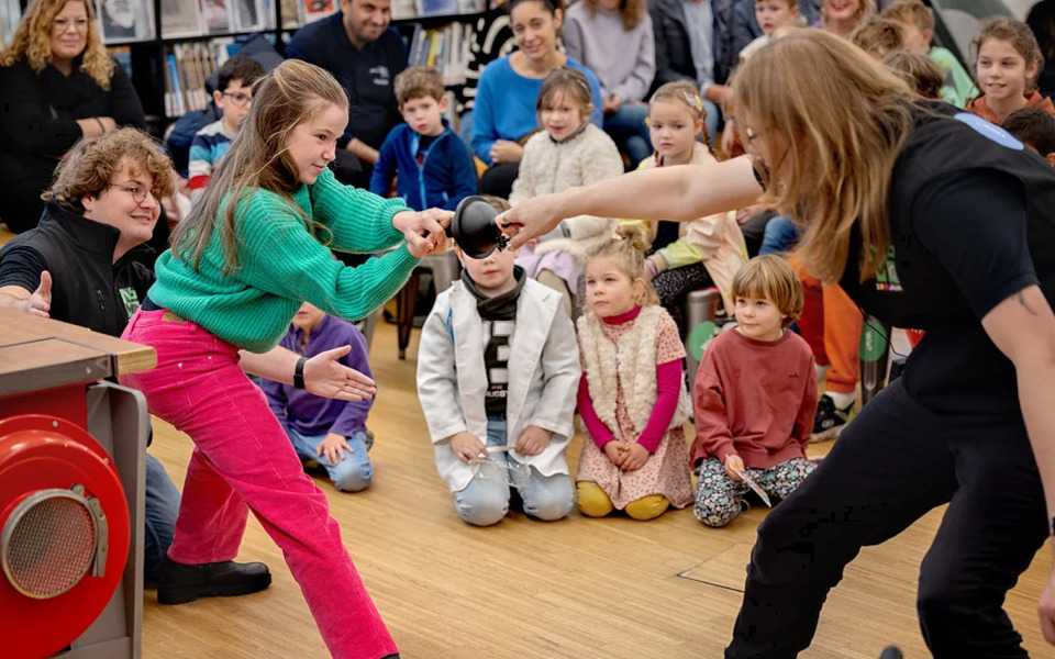 Nemo Science Tour kinderen krijgen een presentatie over techniek en wetenschap, op de voorgrond testen  een medewerker en een kind de trekkracht van een magneet.