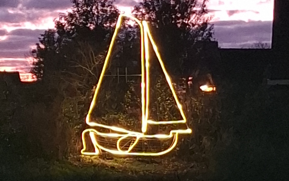Lichtschip De Tsjotter - contouren van een boot met zeilen en een roer verlicht met lichtslangen tegen een begroeide achtergrond