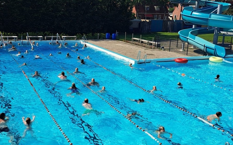 Zwem4daagse zwemmen baantjes openlucht zwembad de sawn stjerren hallum vierdaagse mensen zwemmen baantjes in het zwembad van hallum met op de achtergrond de glijbaan in het blauw