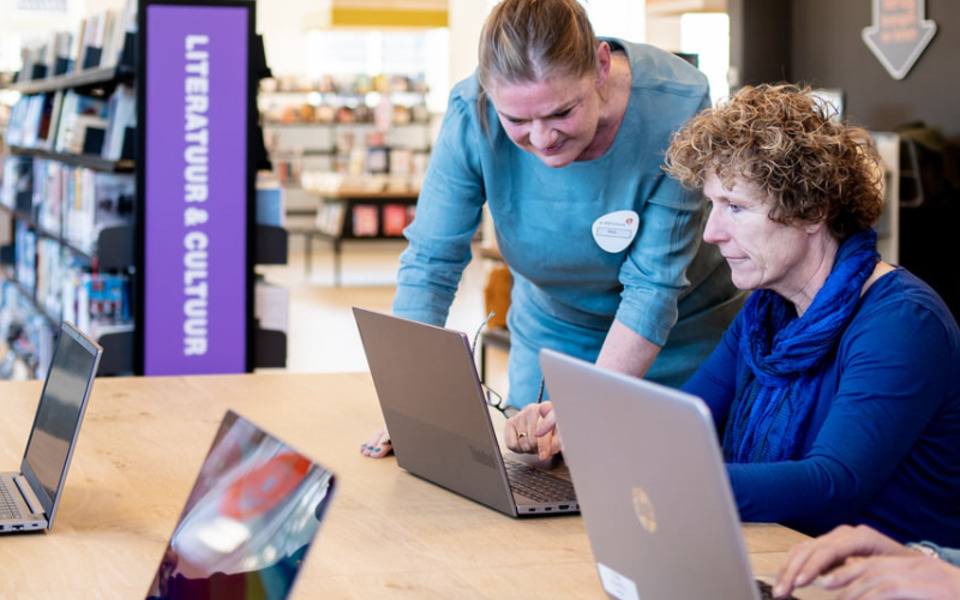 Digi-Taalhuis mensen achter een laptop aan een tafel in de bibliotheek met een vrijwilliger die hulp bied met taal en taalvaardigheid