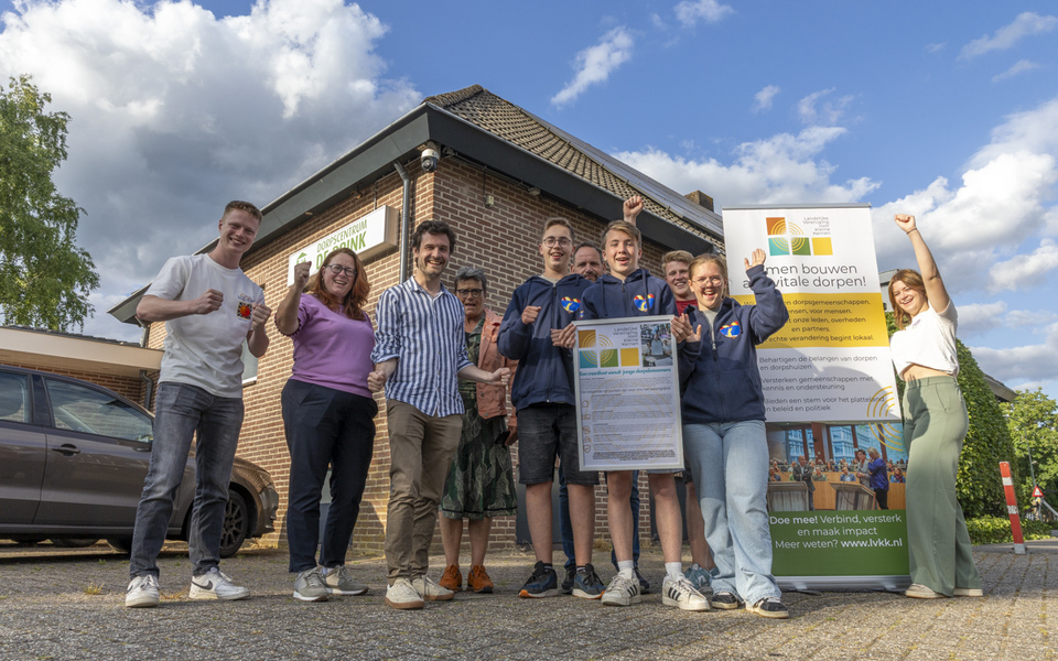 Groep jongeren en volwassenen voor Dorpscentrum De Brink in Loenen, met het manifest en een LVKK-banner, lachend en steun uitend aan het initiatief.