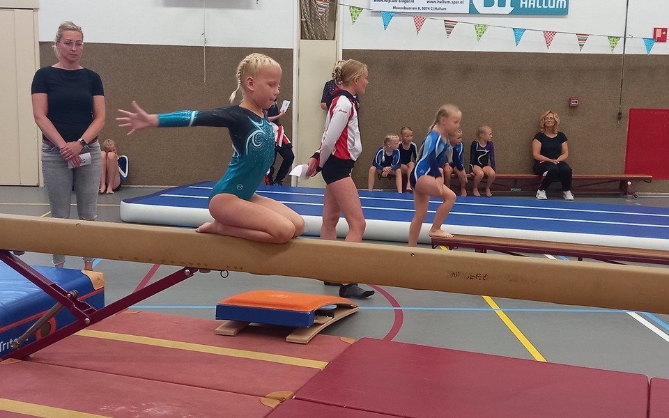 Gym en turnen op de balk en mat in een sportzaal met andere kinderen en trainers in een feestelijke setting met vlaggen