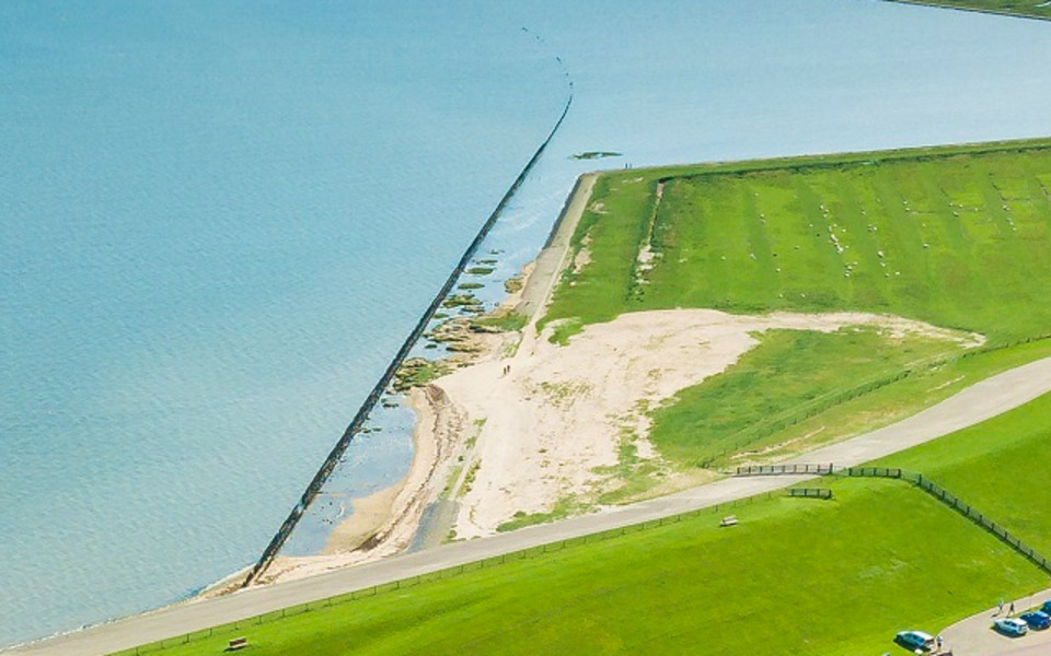 Luchtfoto van de Waddenzeedijk met buitendijks natuurgebied, waar de plannen voor de groene dijk en natuurmaatregelen worden uitgewerkt.