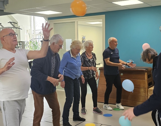 Groep oudere deelnemers doet staand been- en balansoefeningen tijdens de valpreventietraining Ik Sta Sterk.