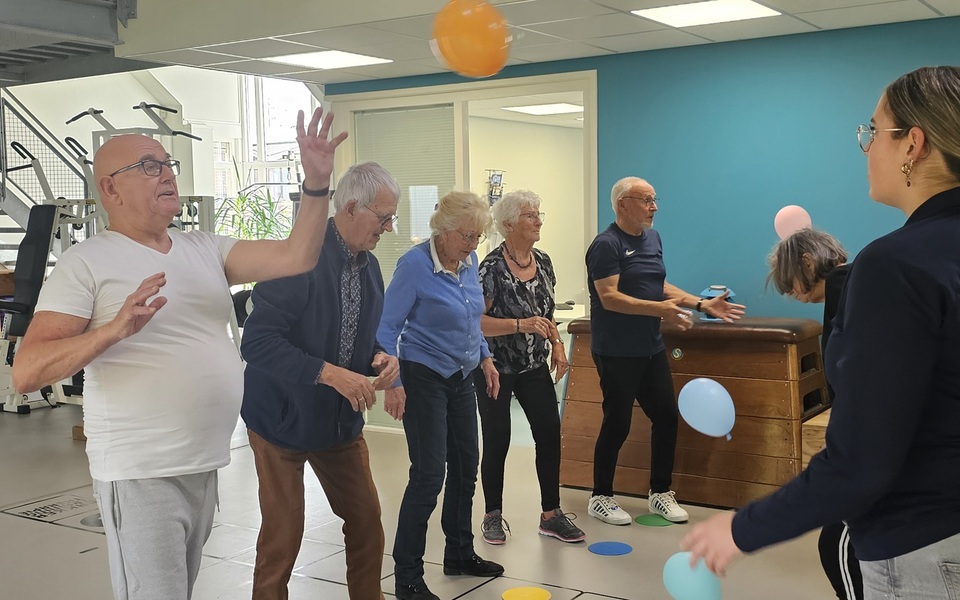 Groep oudere deelnemers doet staand been- en balansoefeningen tijdens de valpreventietraining Ik Sta Sterk.