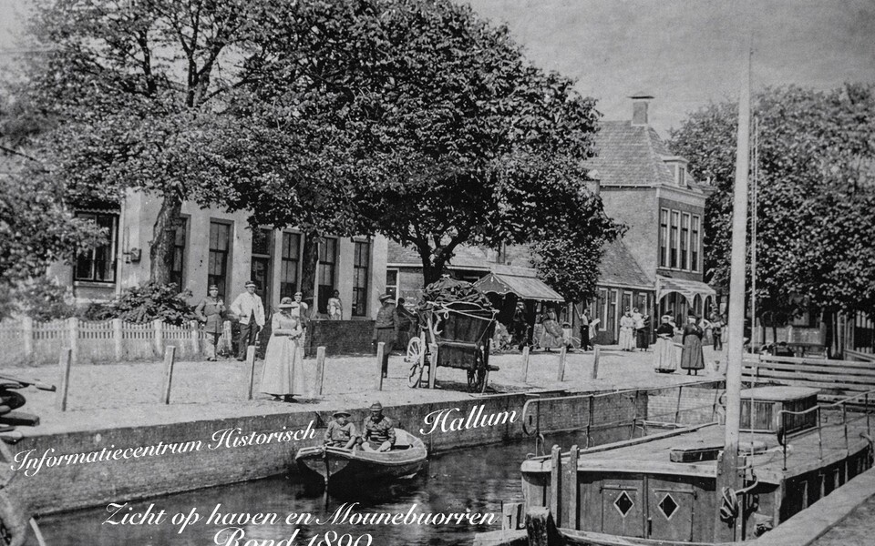 Zwart-witfoto van de Mounebuorren in Hallum rond 1890 met mensen in klederdracht langs de haven, een paard en wagen op de kade en boten in het water.