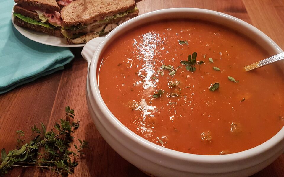 Kom warme tomatensoep met fijngesneden prei bovenop, geserveerd in een witte kom met ingrediënten op de achtergrond.