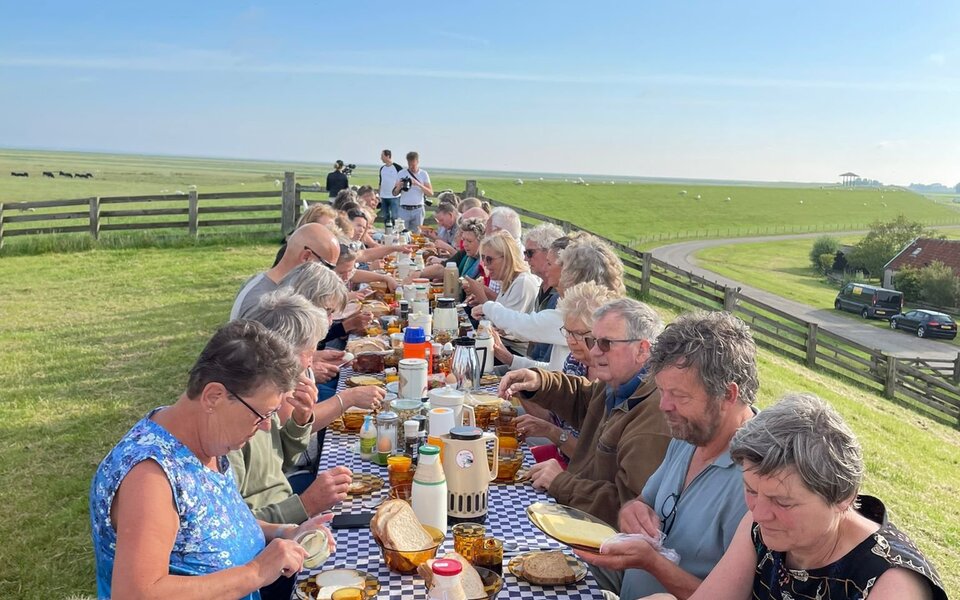 Dorpsgenoten ontbijten samen aan lange tafels op de Waddendijk bij Hallum, met uitzicht over het Friese landschap en de dijk