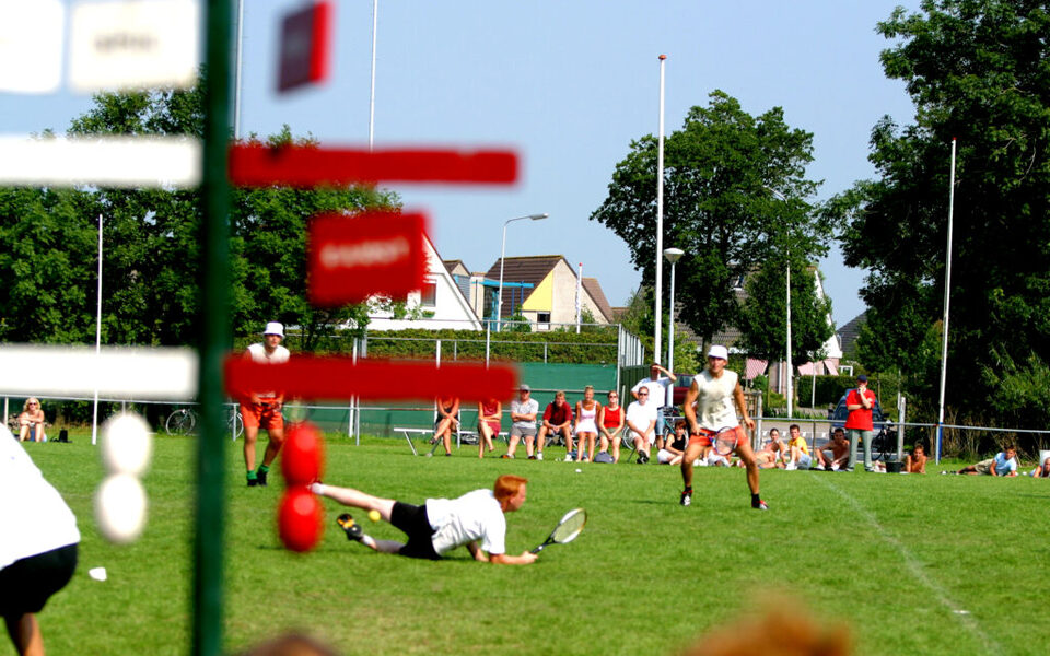 Spelers op het kaatsveld tijdens een potje teatsen, waarbij met tennisrackets en een zachte bal wordt gespeeld.