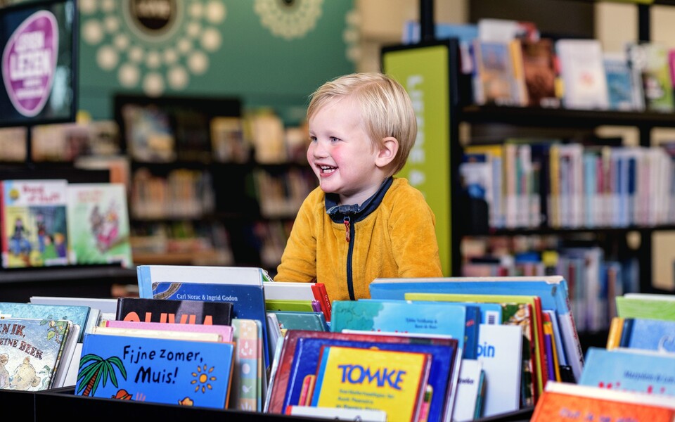 Blij kind tussen kleurrijke kinderboeken in de bibliotheek tijdens een gezellig voorlees- of leesmoment.
